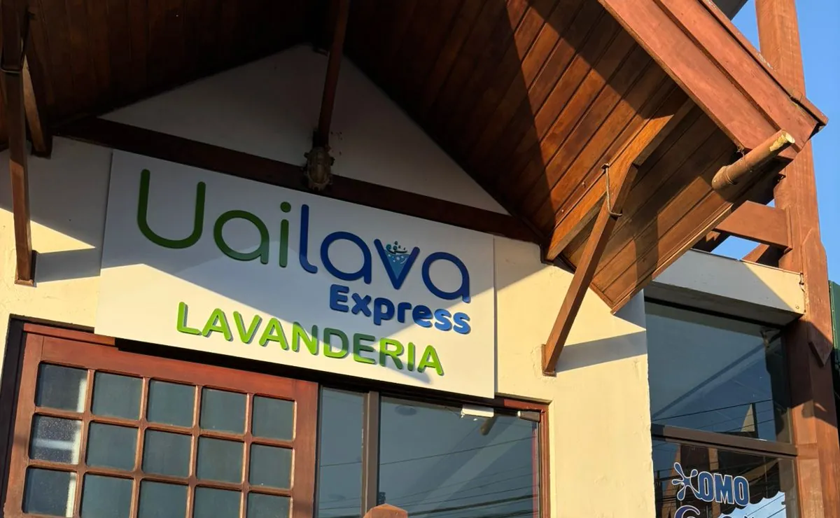 A fachada da Uailava Express Bragança: o letreiro branco com "Uailava Express Lavanderia" sob o telhado de madeira da casa, com o janelão da loja embaixo.
